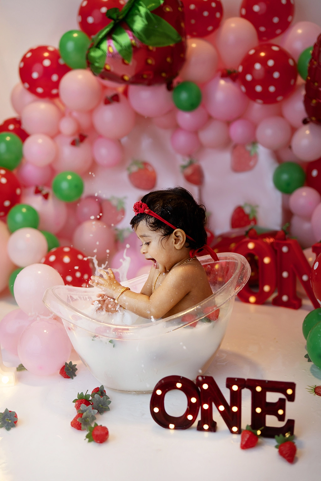 Baby girl enjoying a milk bath after her first birthday photoshoot with a strawberry-themed setup in Enfield, North London