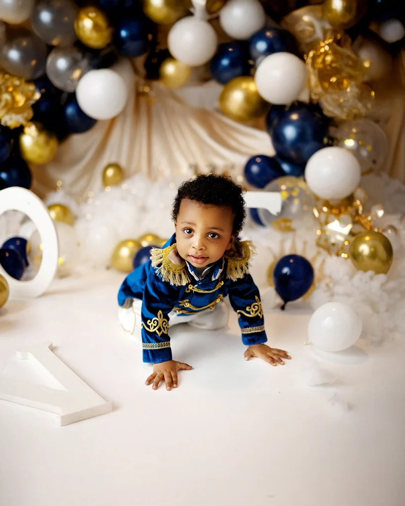Baby boy in a royal blue outfit during a cake smash photography session with blue and gold balloons in Enfield, North London