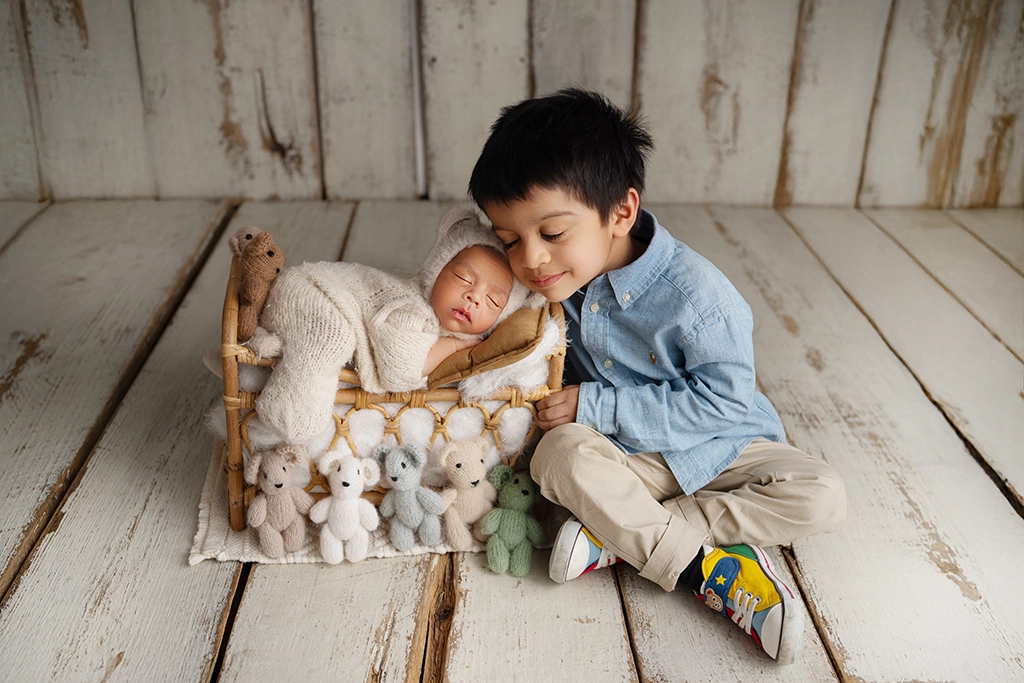 Older brother sitting beside his newborn sibling during a newborn photography session in Enfield, North London