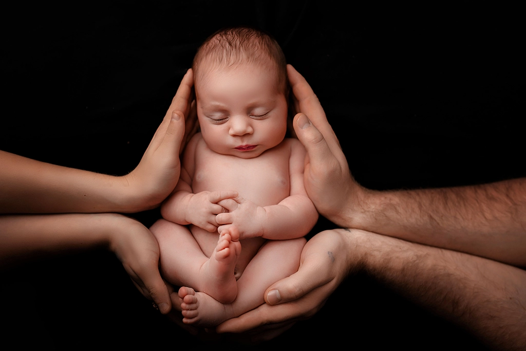 Sleeping newborn baby gently supported by parents' hands during a newborn photography session in Enfield, North London