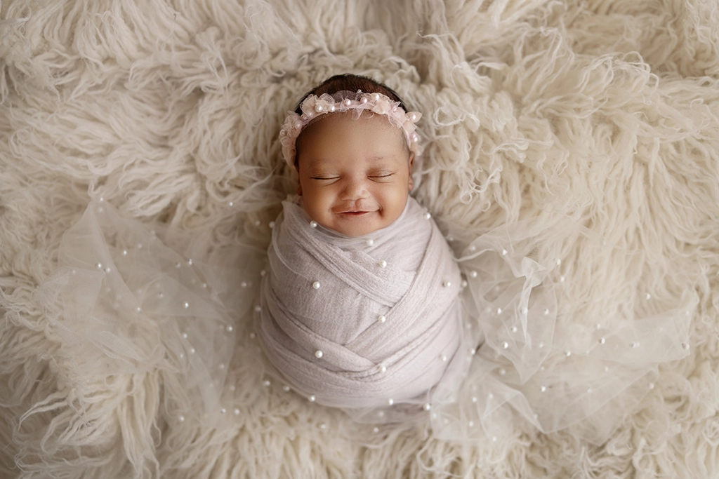 Newborn photography London – smiling baby girl wrapped in pink during her newborn session
