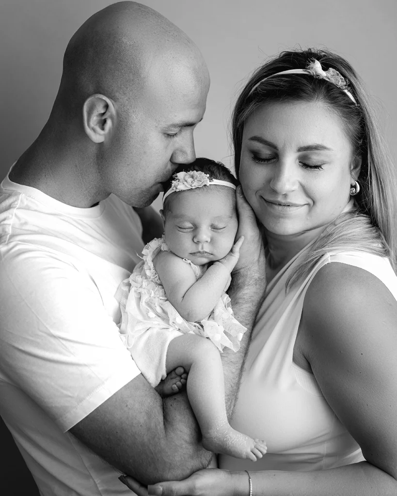 Parents wearing simple white outfits while holding their newborn baby during a newborn family photography session in Enfield, North London