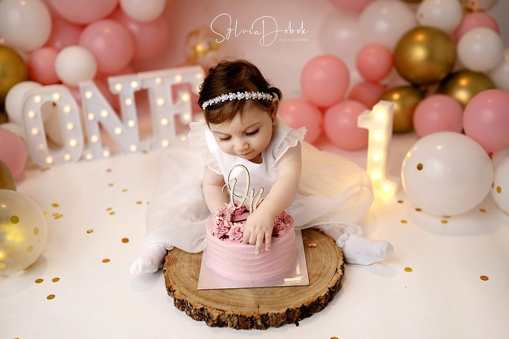 Baby girl celebrating her first birthday with a pink cake during a pink and gold cake smash photography session in Enfield