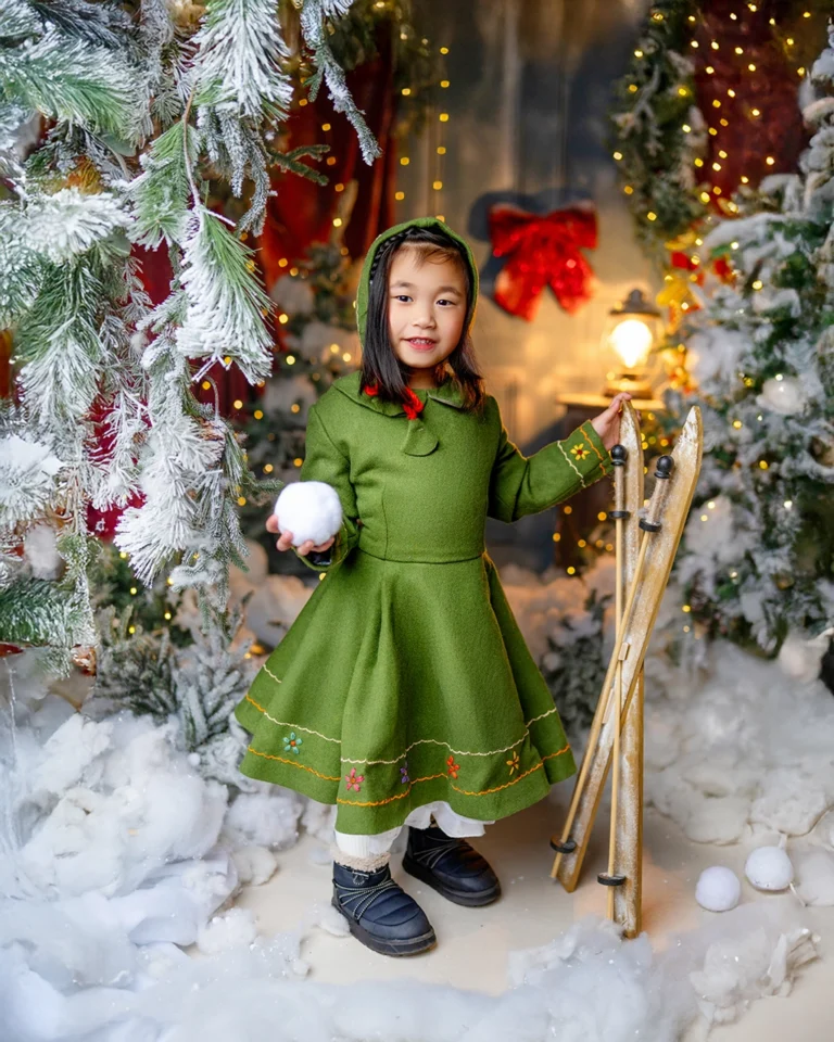 Young girl in a green dress holding a snowball during a Christmas photography session in Enfield, North London