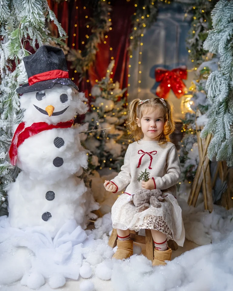 Young girl sitting beside a snowman during a Christmas photography session in Enfield, North London