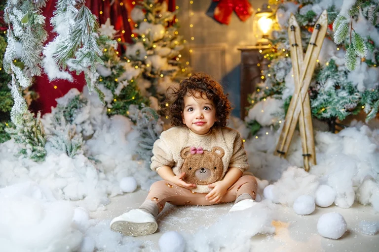 Young child sitting in a snowy Christmas studio setup during a photography session in Enfield, North London