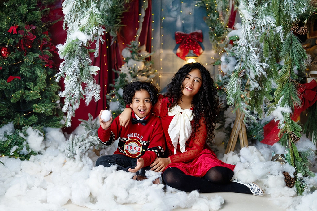 Brother and sister playing together in artificial snow during a Christmas photography session in Enfield, North London