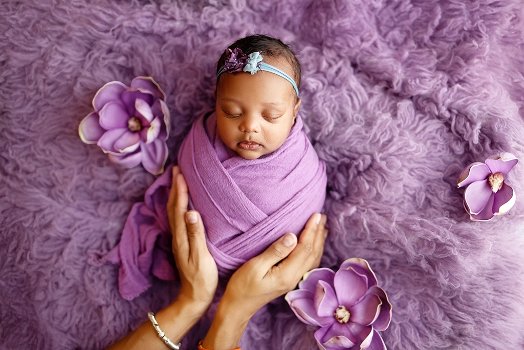Newborn baby wrapped in purple with floral styling during a newborn photography session in Enfield, North London