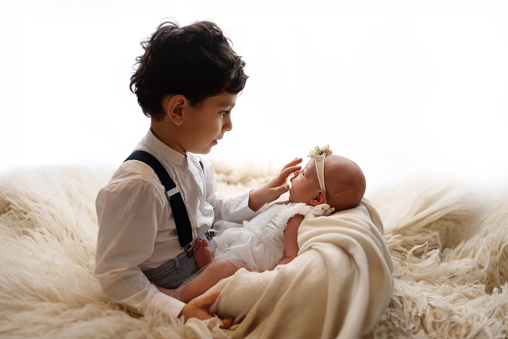 Older sibling gently touching a newborn baby during a newborn photography session in Enfield, North London